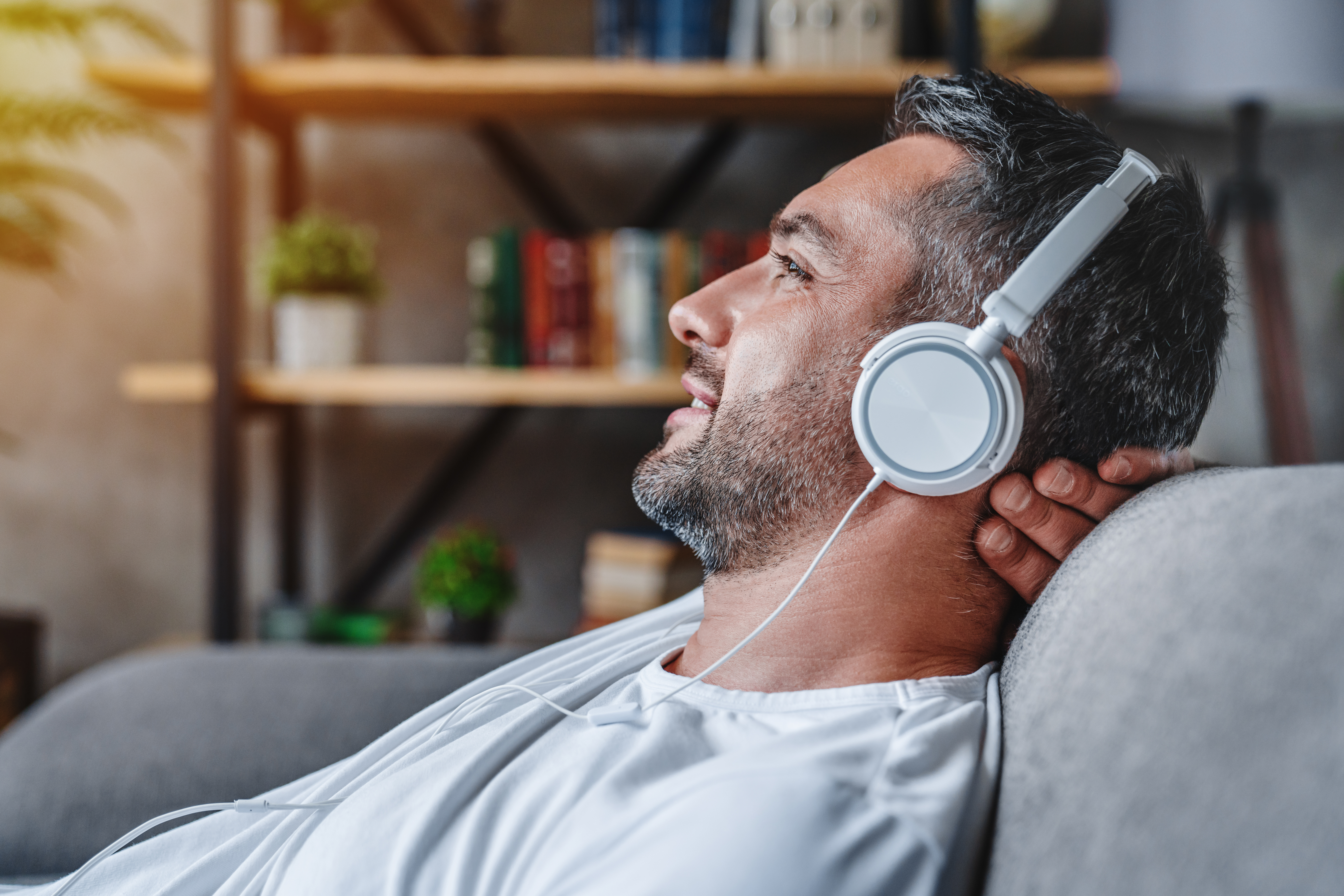 Middle aged man listening music with headphones relaxed in sofa at his home